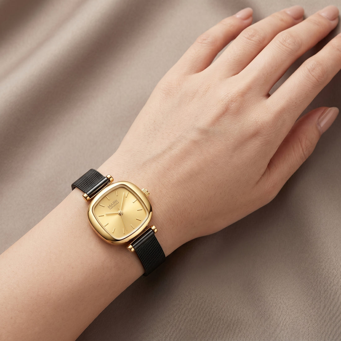 Mark Fairwhale gold-tone watch with black mesh strap on feminine hand