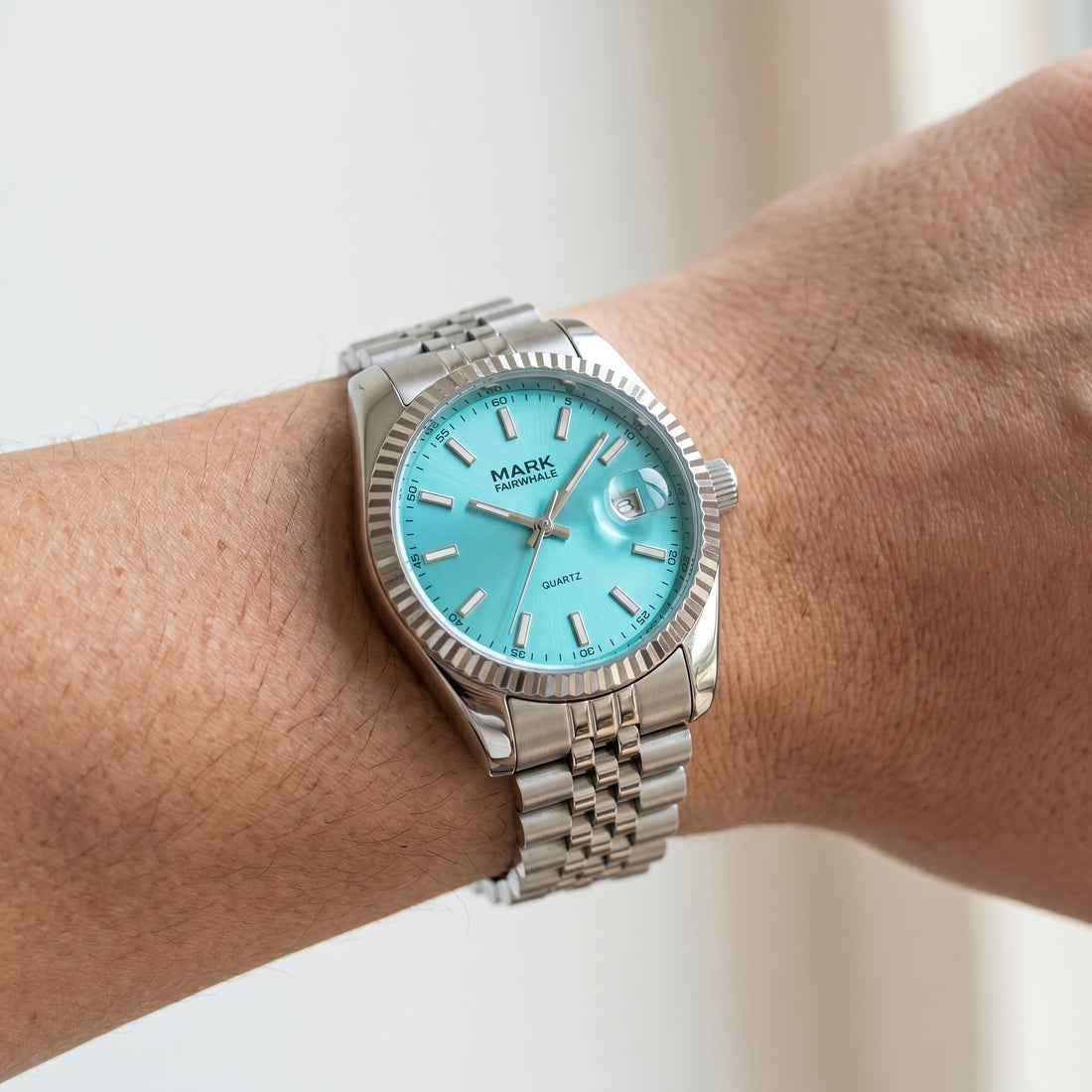 Silver watch with a turquoise dial on a wrist against a white background