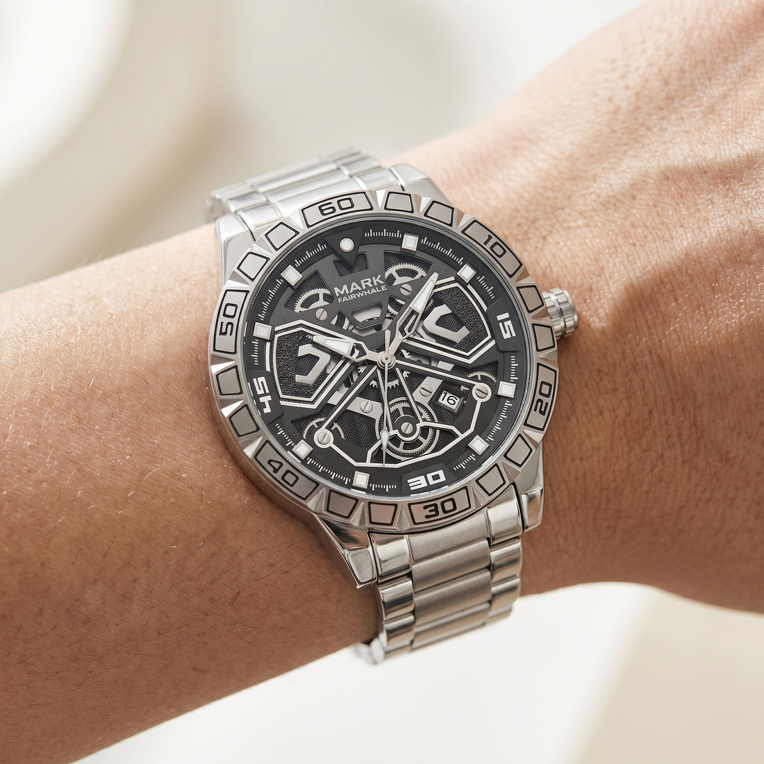 Silver wristwatch with black face on a wrist against a neutral background
