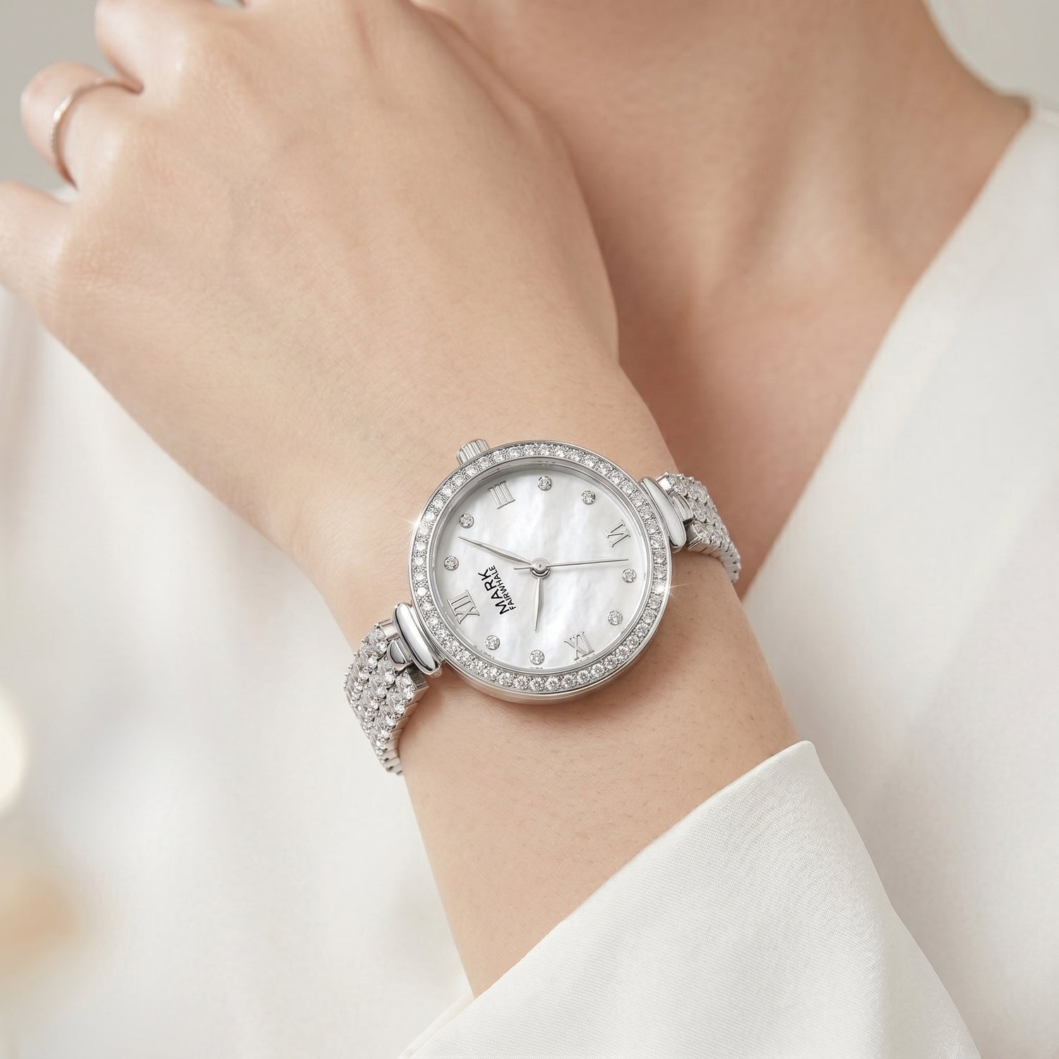 Fairwhale women's minimalist silver watch with diamond bracelet on wrist, clear mother-of-pearl dial detail, elegant ivory outfit