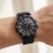 Black wristwatch with a detailed face on a wrist against a neutral background