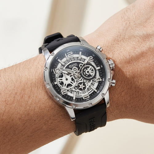 Black wristwatch with a detailed face on a wrist against a neutral background