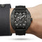 Black wristwatch with detailed design on a person's wrist against a neutral background
