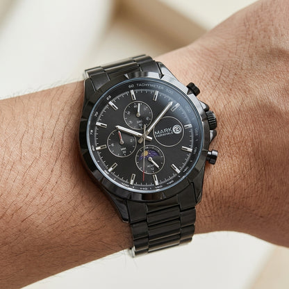 Black wristwatch with detailed face on a wrist against a neutral background