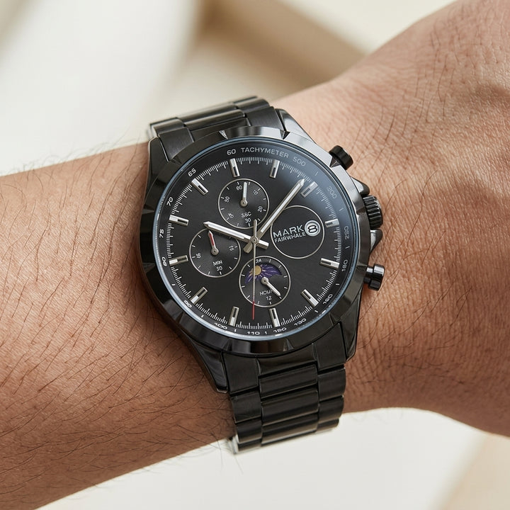 Black wristwatch with detailed face on a wrist against a neutral background