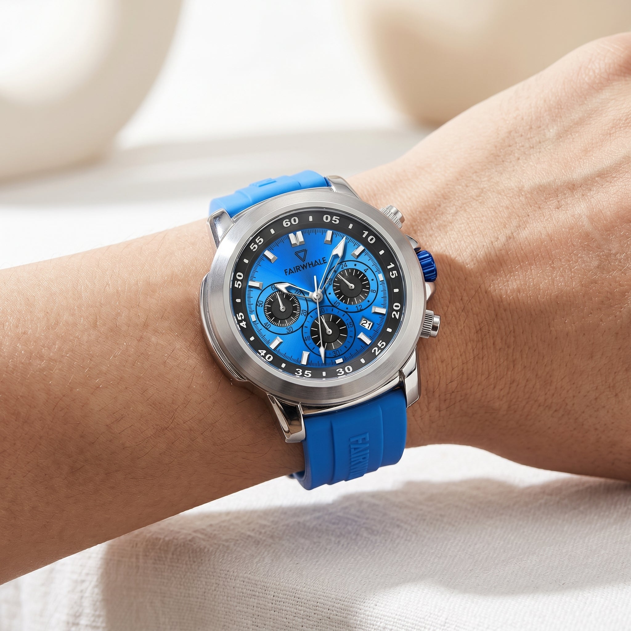Blue watch with silver case on a wrist against a neutral background