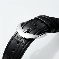 Close-up of a black leather watch strap with a silver buckle on a light gray background