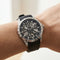 Close-up of a wrist wearing a black wristwatch with a detailed face.