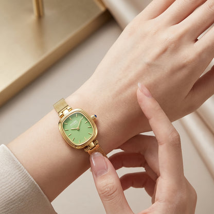 Gold watch with a green face on a wrist, held by a hand