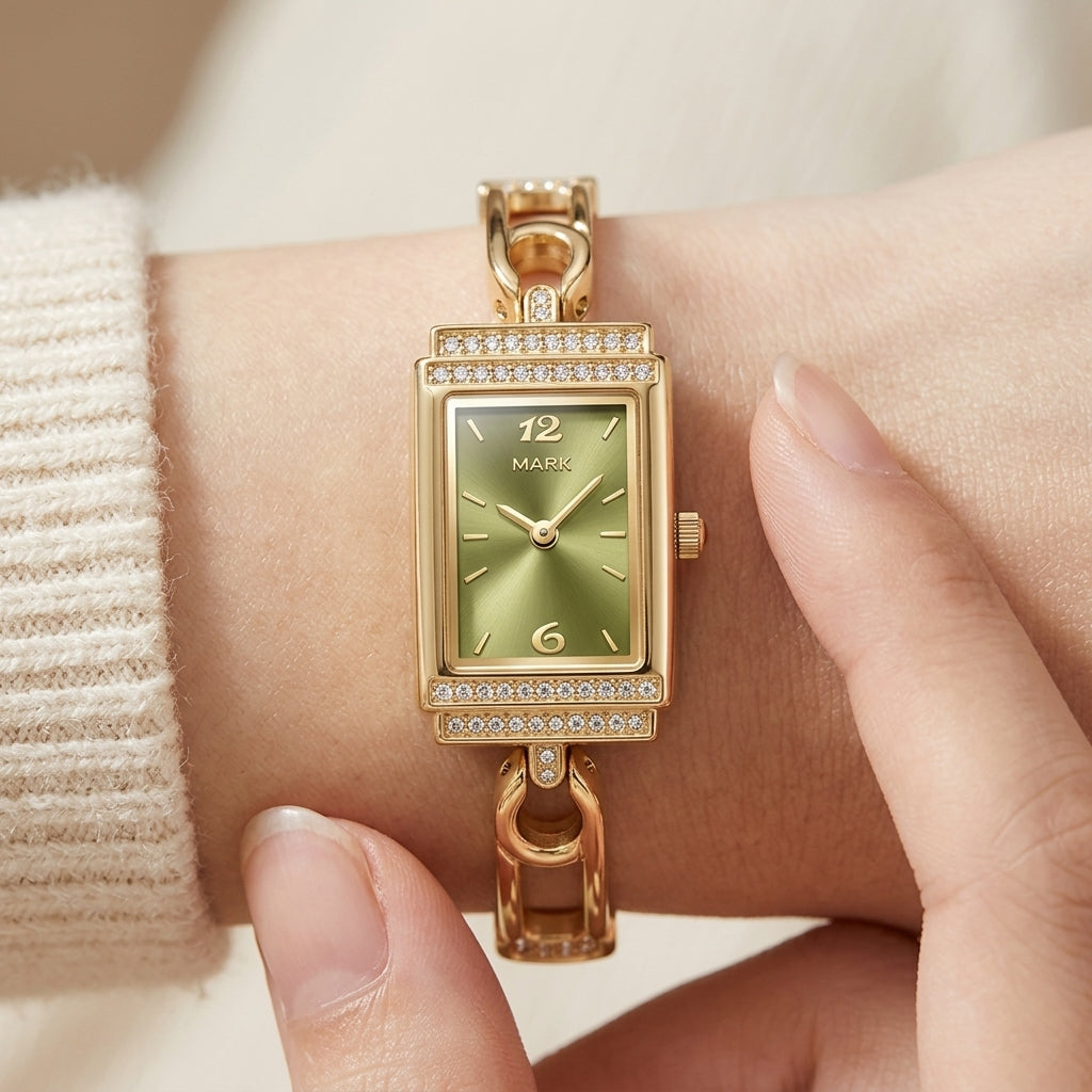 Gold wristwatch with green face on a wrist, wearing a beige sweater.