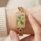 Gold wristwatch with green face on a wrist, wearing a beige sweater.