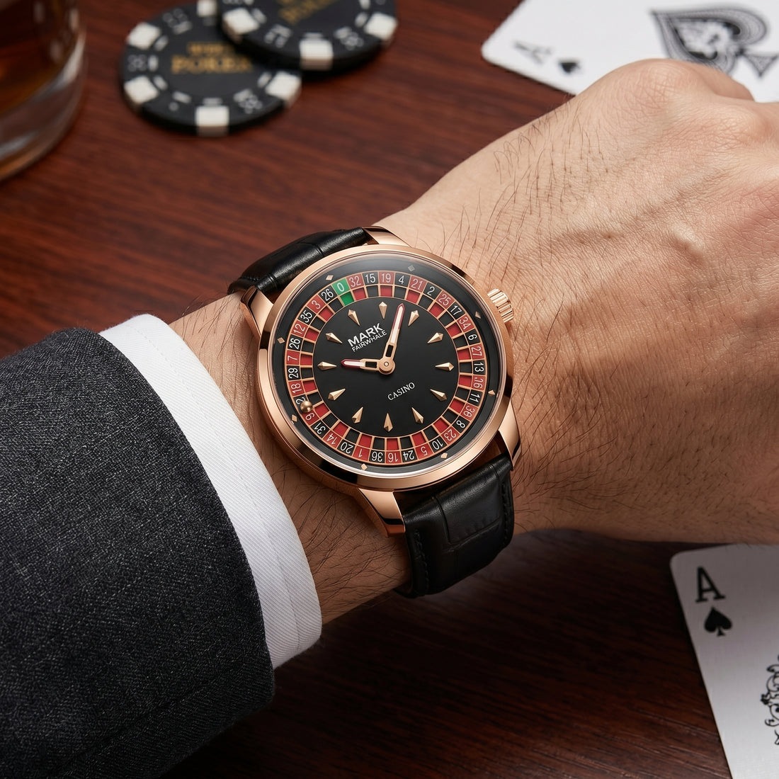 Luxury watch with a detailed face on a wrist, surrounded by playing cards and a glass of whiskey.