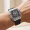 Luxury watch with black strap and silver case on a wrist against a neutral background