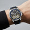 Luxury watch with black strap and visible mechanical components on a wrist against a gray background