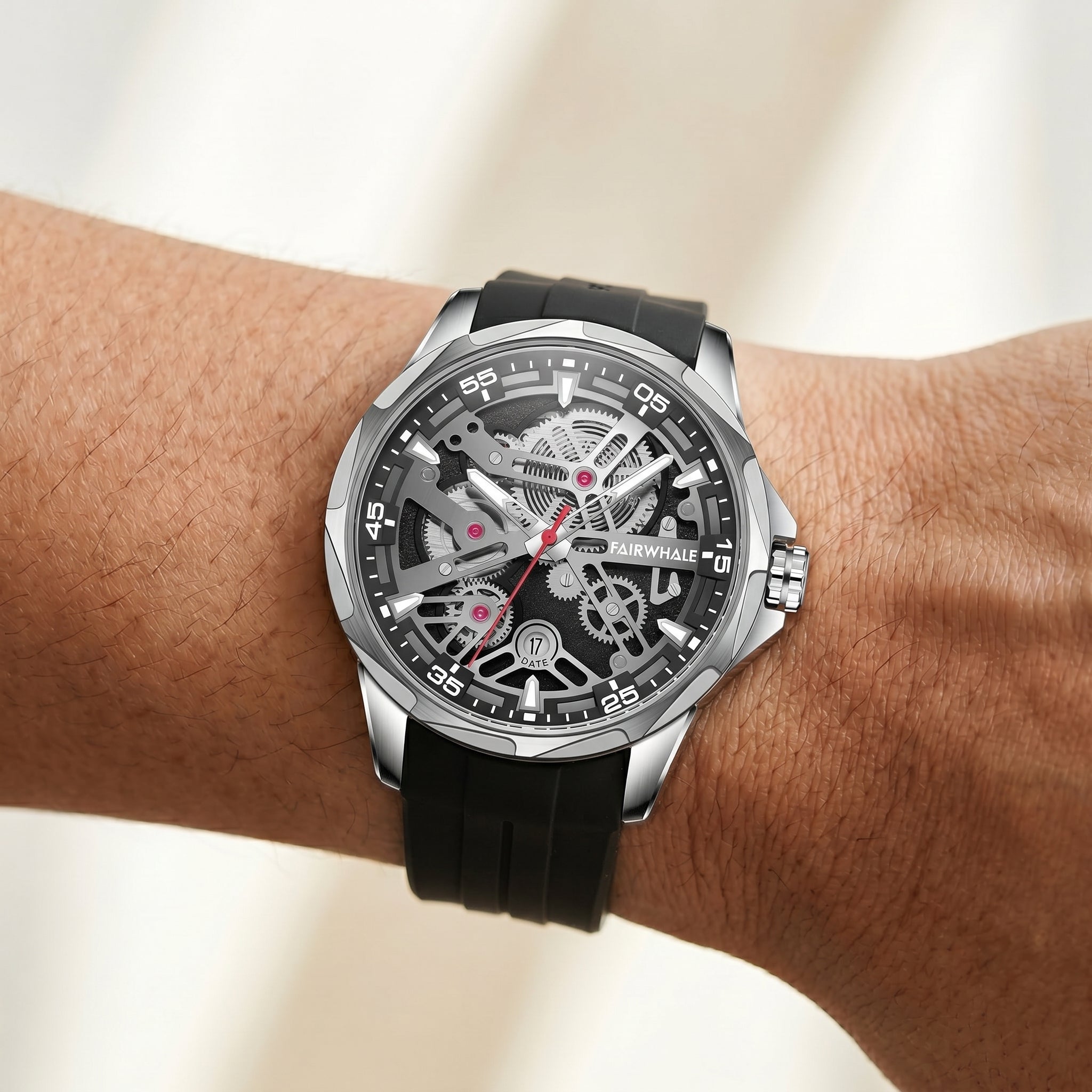 Mechanical wristwatch with black strap on a person's wrist against a neutral background