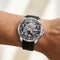 Mechanical wristwatch with black strap on a person's wrist against a neutral background