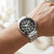 Silver watch with a black face on a wrist against a blurred background