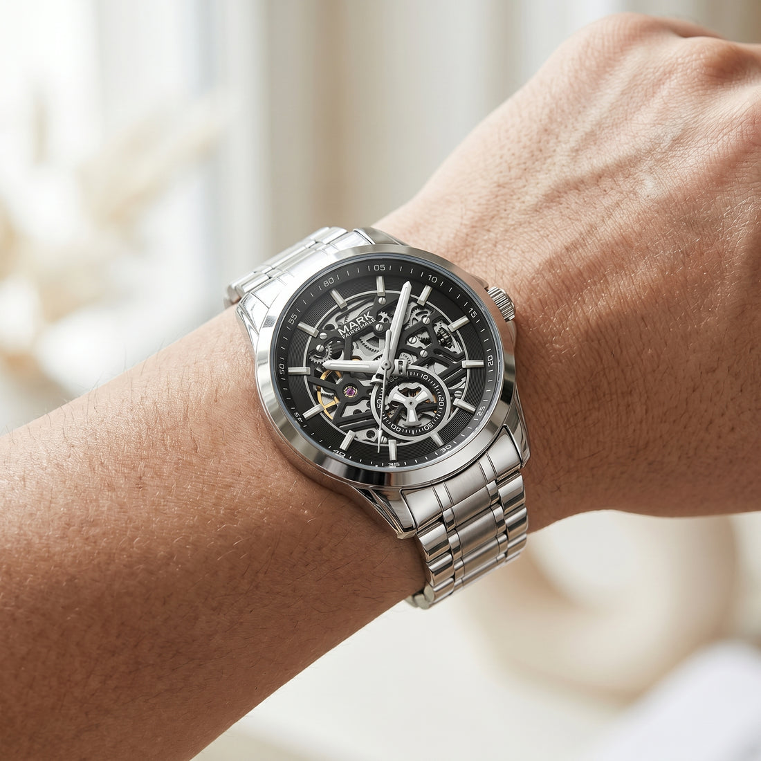 Silver watch with a black face on a wrist against a blurred background