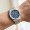 Silver watch with a blue face on a wrist against a neutral background