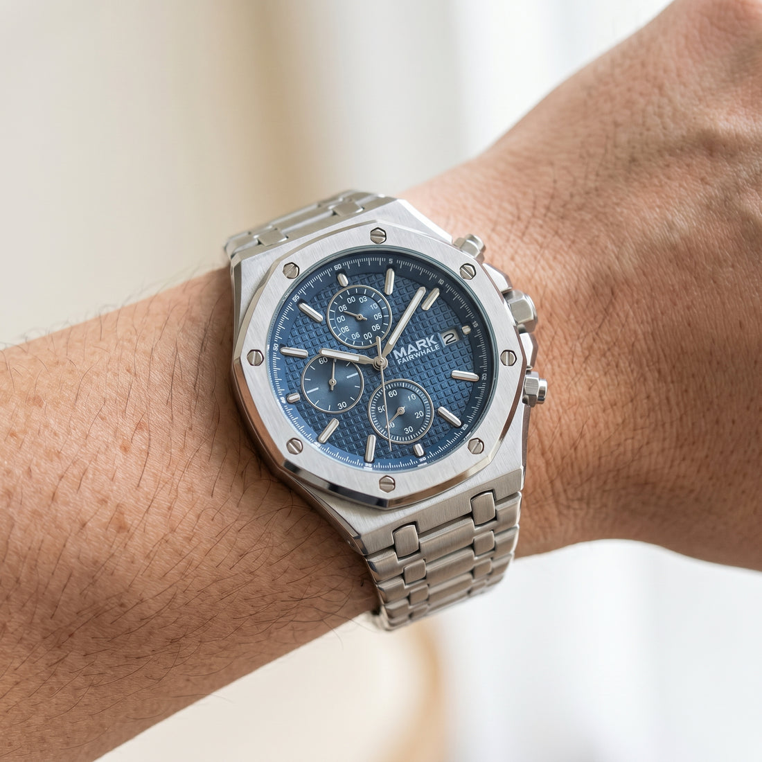 Silver watch with a blue face on a wrist against a neutral background