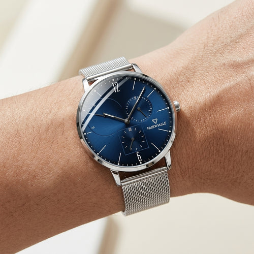 Silver watch with a blue face on a wrist against a neutral background