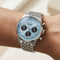 Silver watch with a blue face on a wrist against a neutral background