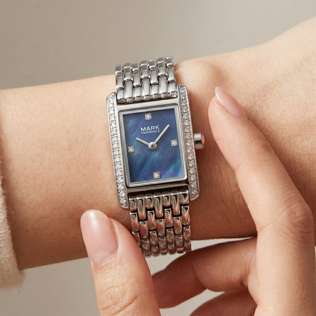 Silver watch with a blue face on a wrist against a neutral background