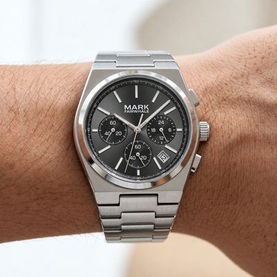 Silver watch with a dark face on a wrist, brand 'Mark Fairwhale' visible