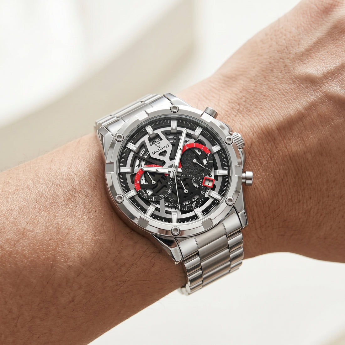 Silver watch with black face and red accents on a wrist against a neutral background