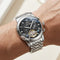 Silver wristwatch with detailed face on a wrist against a neutral background