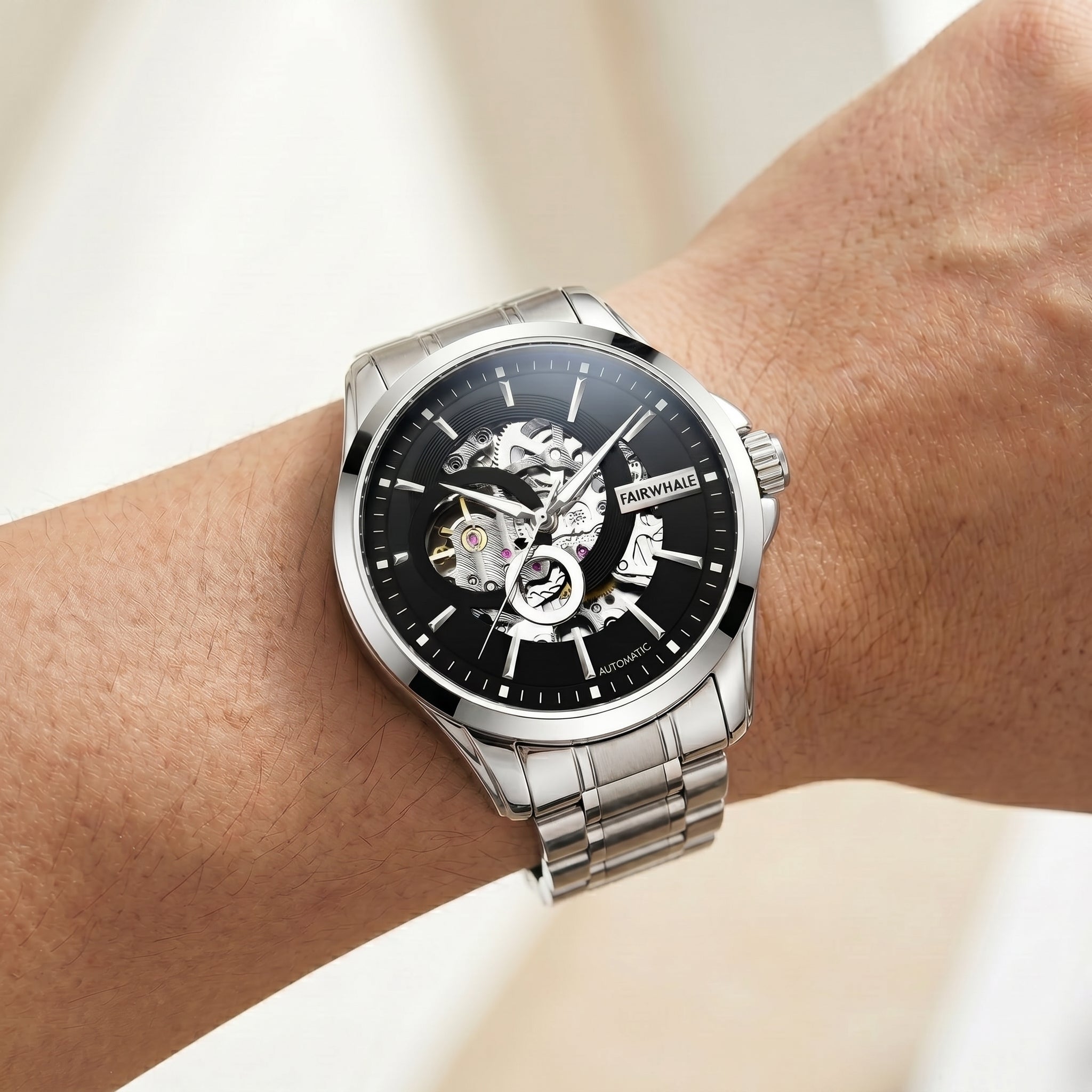 Silver wristwatch with black face on a wrist against a neutral background