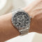 Silver wristwatch with black face on a wrist against a neutral background
