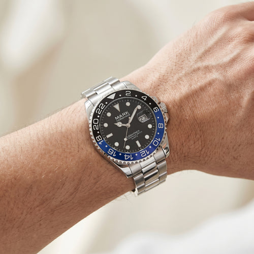 Watch with a black face and blue accents on a wrist against a neutral background