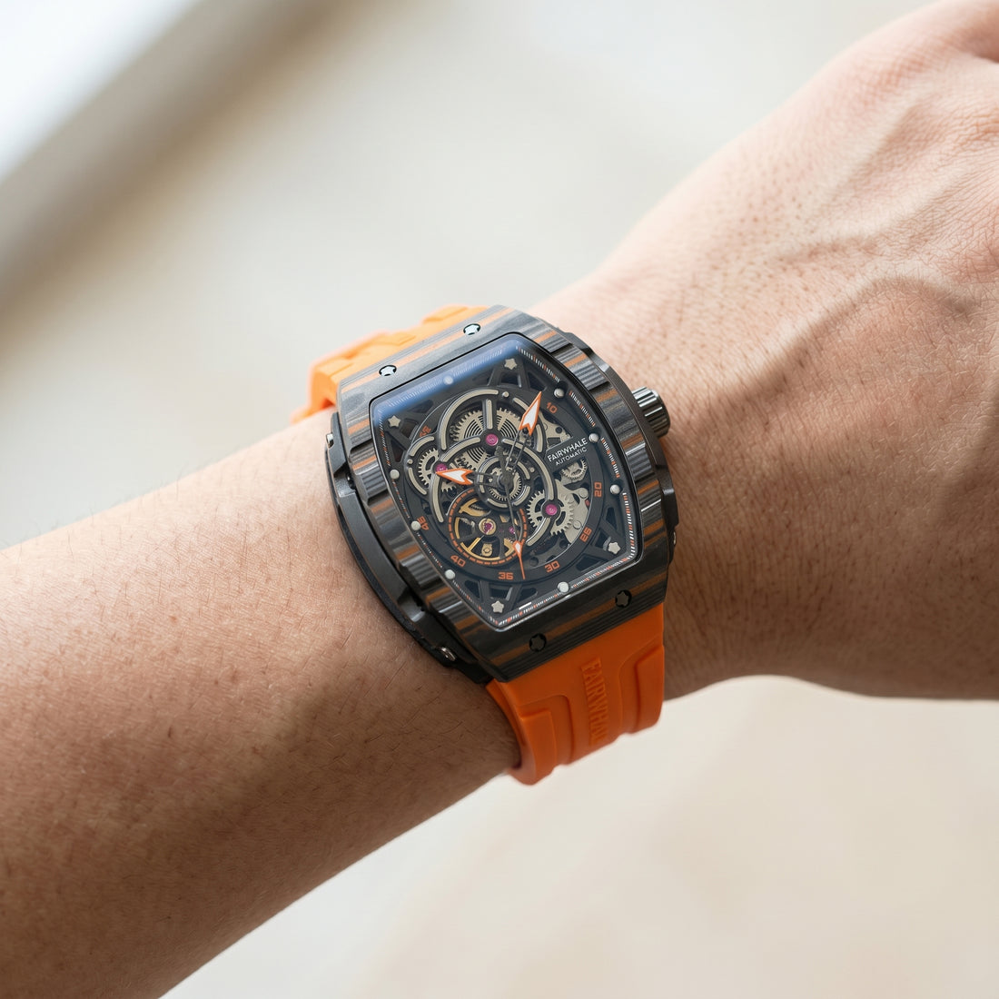 Watch with an orange strap on a wrist against a neutral background