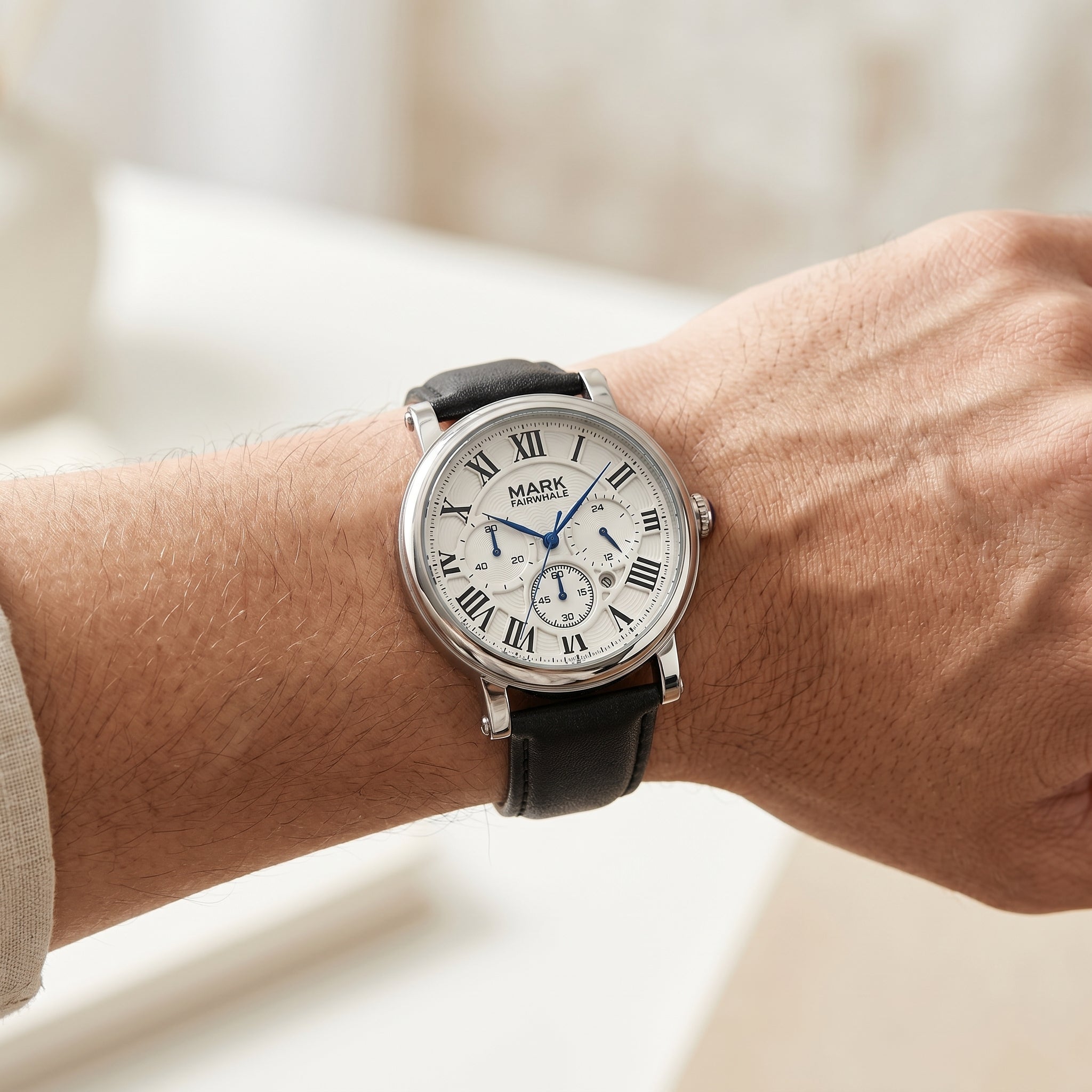 Wrist wearing a silver watch with black leather strap on a blurred background