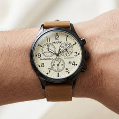Wrist wearing a watch with a brown leather strap and white face on a light background