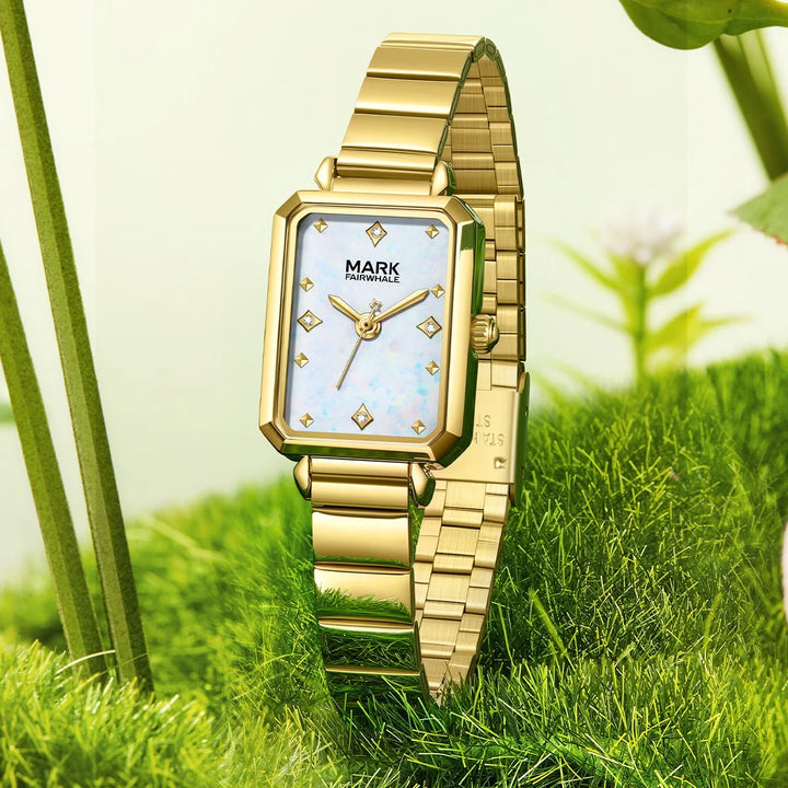 Mark Fairwhale FW-3070 ALERIA Women’s Square Quartz Watch with white mother-of-pearl dial and gold bracelet, standing on natural background.