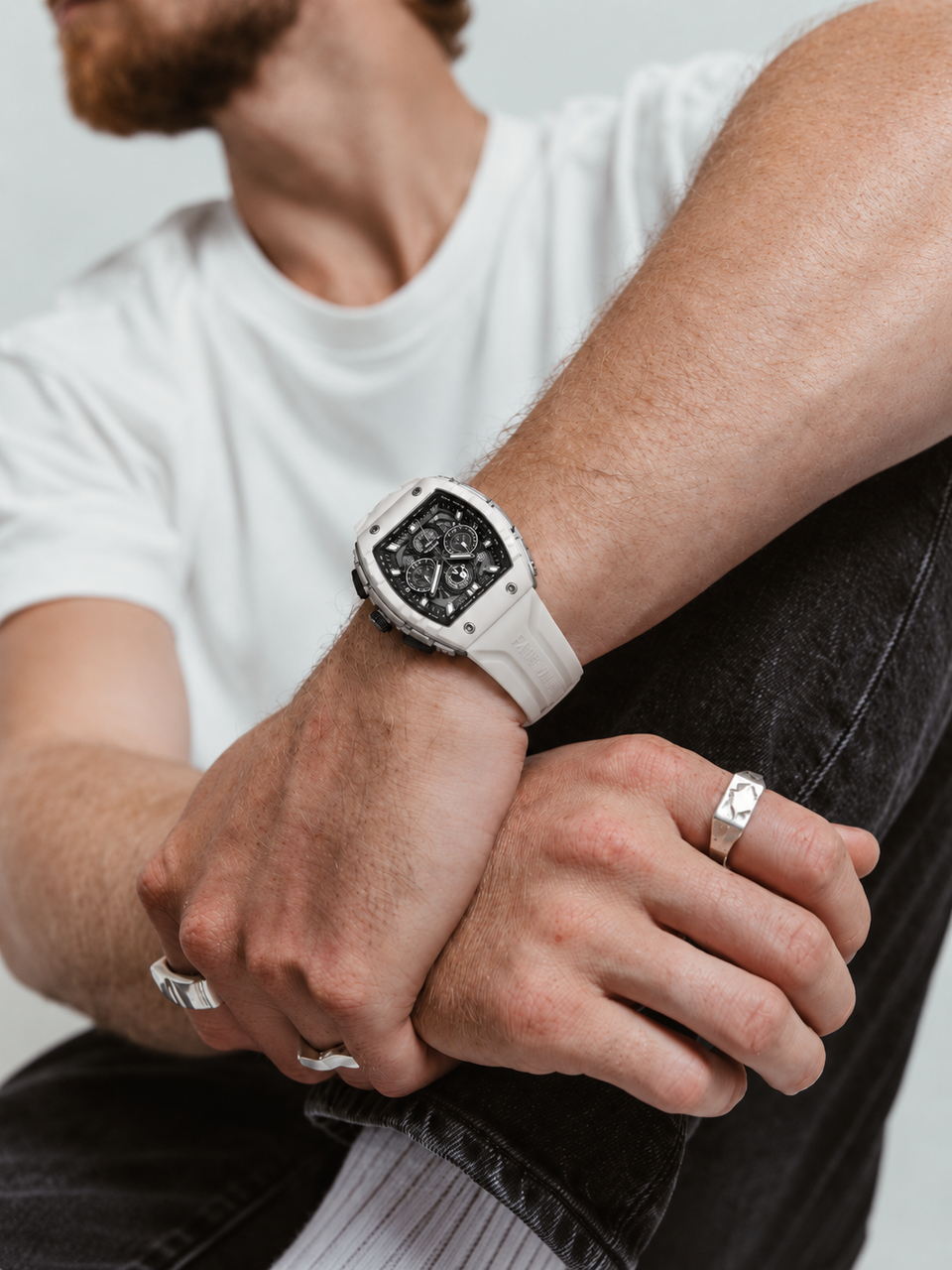 BOLTRON in White on the wrist of a seated man in a white tee and black jeans, hands crossed over one knee