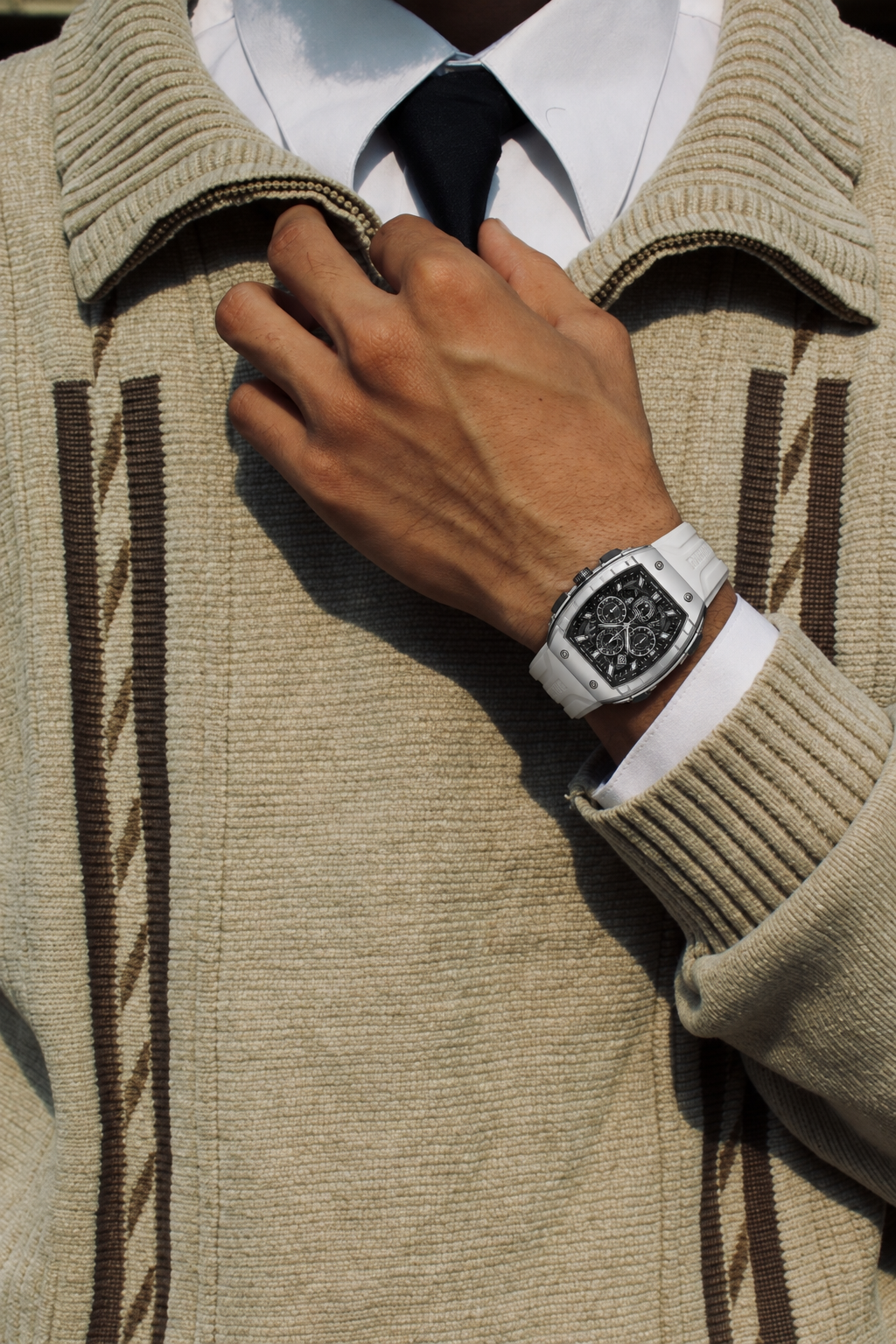 BOLTRON in White on a hand adjusting the collar of a beige knit cardigan, over a white shirt and dark tie