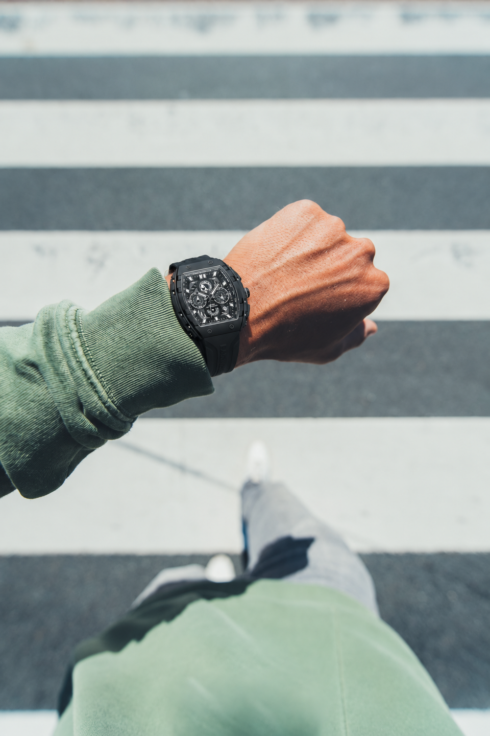 BOLTRON in Black on the wrist of a man in a green sweatshirt, seen from above as he crosses a crosswalk